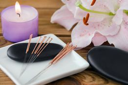 Acupuncture needles with a lit candle and flower on a wooden table.