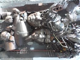 Escultura de metal con formas humanas abstractas y elementos mecánicos entrelazados.