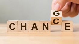Blocs en bois formant les mots "CHANCE" et "CHANGE" avec une main ajustant un bloc.