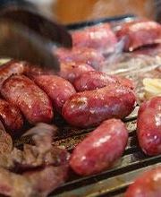 Churrasco com linguiças e carne na grelha. Mão usando pinça para virar a carne.