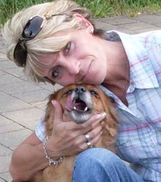 Frau kuschelt mit einem kleinen, braunen Hund auf einem gepflasterten Weg.