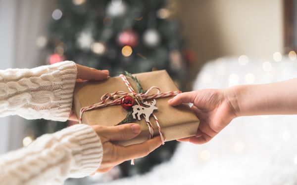 Eine Person reicht einer anderen ein weihnachtlich verpackts Geschenk.