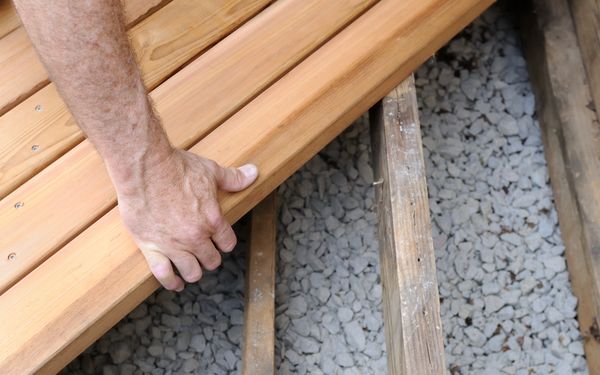 Mann entfernt ein paar Holzbretter seiner Terrasse, um zu sehen, ob sich darunter Schimmelbefall feststellen lässt.