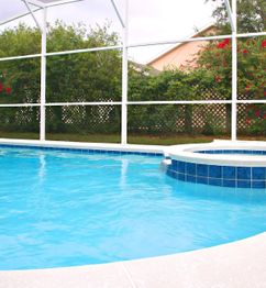 Outdoor pool and spa surrounded by greenery and a screen enclosure.
