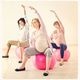 Drie zwangere vrouwen doen rek- en strekoefeningen op roze fitnessballen in een lichte zaal.