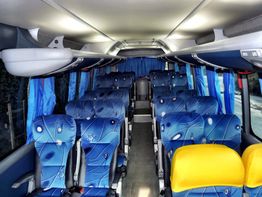 Interior de um ônibus vazio com poltronas azuis e cortinas da mesma cor.