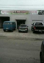 Loja de peças e mecânica com três carros estacionados na frente, incluindo uma Kombi azul.