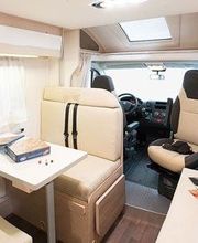 Interior de una autocaravana con asientos beige, mesa pequeña y volante a la vista.