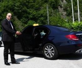 Ein Mann im Anzug öffnet die Tür eines schwarzen Autos mit Taxischild.