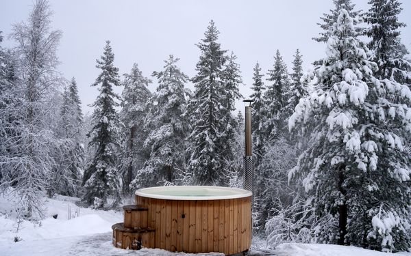 Ein Badefass aus Holz steht in einer eingeschneiten Winterlandschaft.