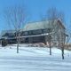 Large house on a snowy hill with bare trees and a clear blue sky.