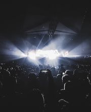 Un concerto pieno di folla con luci brillanti sul palco in un'atmosfera scura e intensa.