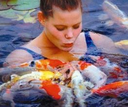 Eine Frau im Wasser küsst Koi-Fische. Sie trägt ein Haarband. Text: "Kiss your Koi".
