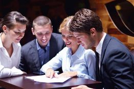 Four people in business attire reviewing a document together at a table.