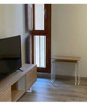 Sala con televisor, mesa pequeña, cama y ventana de madera. Decoración minimalista y moderna.