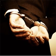 Person in a suit handcuffed with hands behind their back.