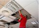 Person in red shirt fixing ceiling panels in an office building.