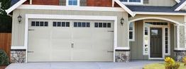 Modern house with beige garage door and front entrance, featuring small windows and stone accents.