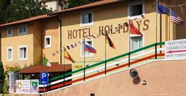 Edificio giallo con insegna "Hotel Holidays" e bandiere nazionali sulla facciata.