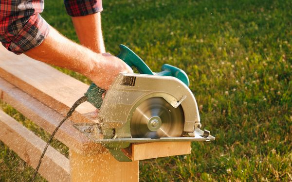 Auf einer Wiese wird eine Holzdaube wird mit einer Kreissäge von einer Person zugeschnitten