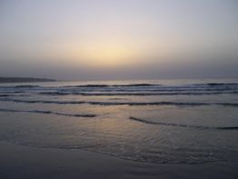 Sonnenuntergang am Strand mit sanften Wellen und einem hellen Himmel im Hintergrund.