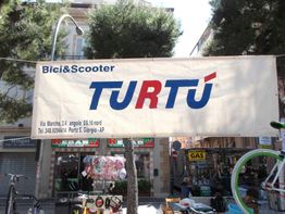 Striscione di promozione per "Turtù", negozio di bici e scooter, su una strada alberata.