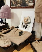 Beige Accessoires auf Holztisch: Hut, Handschuhe, Hausschuhe, Pullover und Hundebild im Hintergrund.