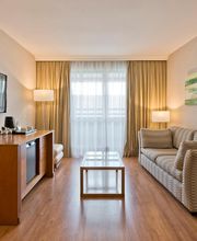 Sala moderna com sofá, TV, mesa de vidro, luminárias e cortinas, decorada com uma planta.