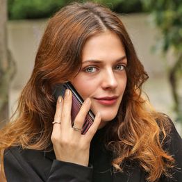 Eine Frau mit langen Haaren telefoniert draußen mit einem Smartphone.