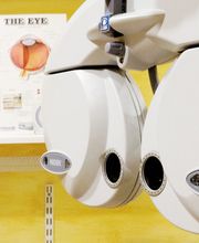 Equipo de optometría con gráfico ocular de fondo en una sala de examen visual.