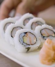 Plato de sushi con camarón, acompañado de jengibre encurtido y una mano al fondo.