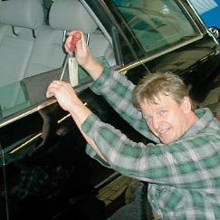 Mann öffnet ein Auto mit speziellem Werkzeug, lächelt dabei.
