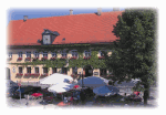 Gebäude mit rotem Dach und grüner Rankenverzierung, umgeben von einem sonnigen Außenbereich.