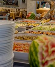 Buffet com pratos diversos decorados com melancias esculpidas e pilha de pratos ao lado.