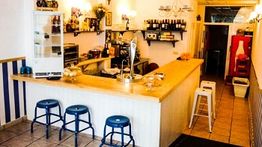 Pequeño café con barra de madera, taburetes azules y decoración acogedora.