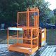 Orange Hebebühne auf gepflastertem Platz, im Hintergrund Bäume und geparkte Autos.