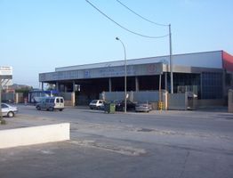 Edificio industrial con coches aparcados al frente y cielo despejado.