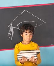 Niño con libros frente a una pizarra con dibujo de birrete de graduación. Fondo azul.