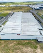 Vista aérea de um grande galpão industrial em um parque logístico com estradas ao redor.
