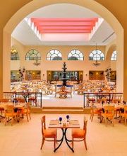 Comedor amplio con arco, techo rosado, mesas elegantes y fuente central.