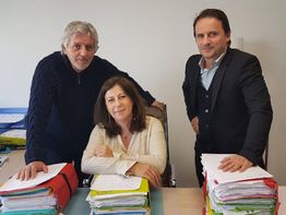 Trois personnes posant autour d'un bureau avec des piles de documents.