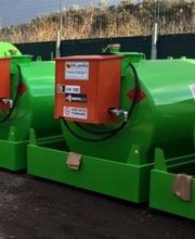 Serbatoi verdi con pannelli arancioni allineati all'aperto su terra battuta.