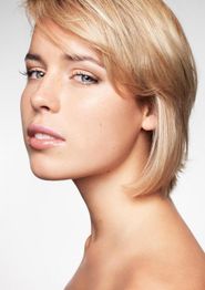 Eine Frau mit kurzem blondem Haar schaut ernst zur Seite, vor weißem Hintergrund.