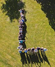 Menschen formen ein "L" auf einer Wiese aus der Vogelperspektive.