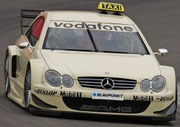 Mercedes-Benz Rennwagen mit "Taxi"-Schild, Sponsorenlogos, in Fahrt auf der Rennstrecke.
