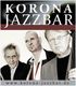 Drei Musiker posieren vor einem "Korona Jazzbar"-Banner, Webseite unten: korona-jazzbar.de.