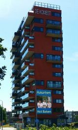 Hoog gebouw "De Komeet" met reclameposter voor huisartsenpraktijk "Het Baken" aan de zijkant.