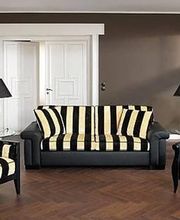 Wohnzimmer mit gestreiftem Sofa, zwei Sesseln, zwei Lampen und Holzboden. Wandfarbe ist braun.