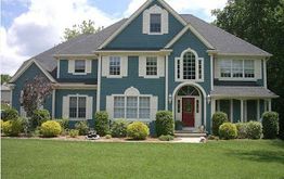 Two-story blue house with white trim, arched entry, red door, and well-kept lawn and shrubs.