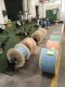 Spools of colored cables in a factory setting with machinery in the background.